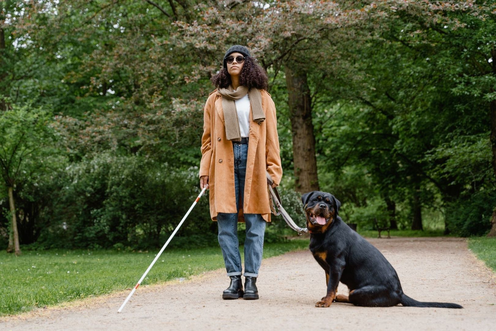 Person mit Langstock und Rottweiler an der Leine im Park